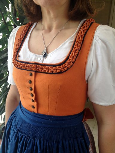 Frau in traditioneller Tracht mit orangefarbenem Oberteil und blauer Rock.
