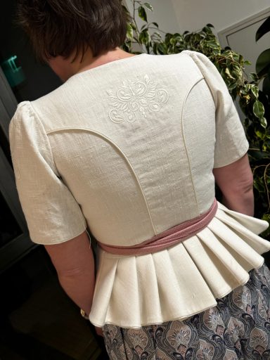 Rückansicht eines eleganten, weißen Oberteils mit Rüschendetails und einem rosa Gürtel.