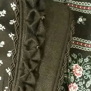 Detailaufnahme von schwarzem Stoff mit Rüschen und floralem Muster.